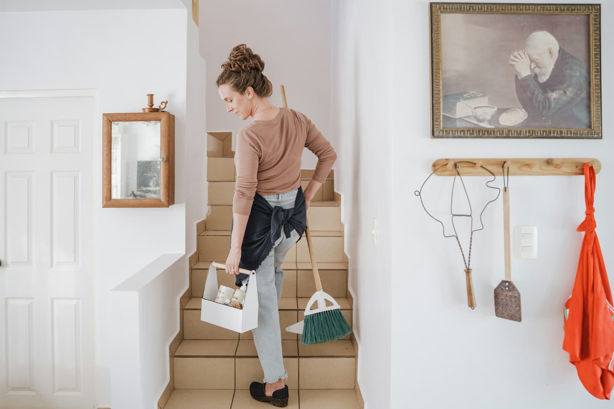 Cleaner carrying a caddy and brush up a bright staircase