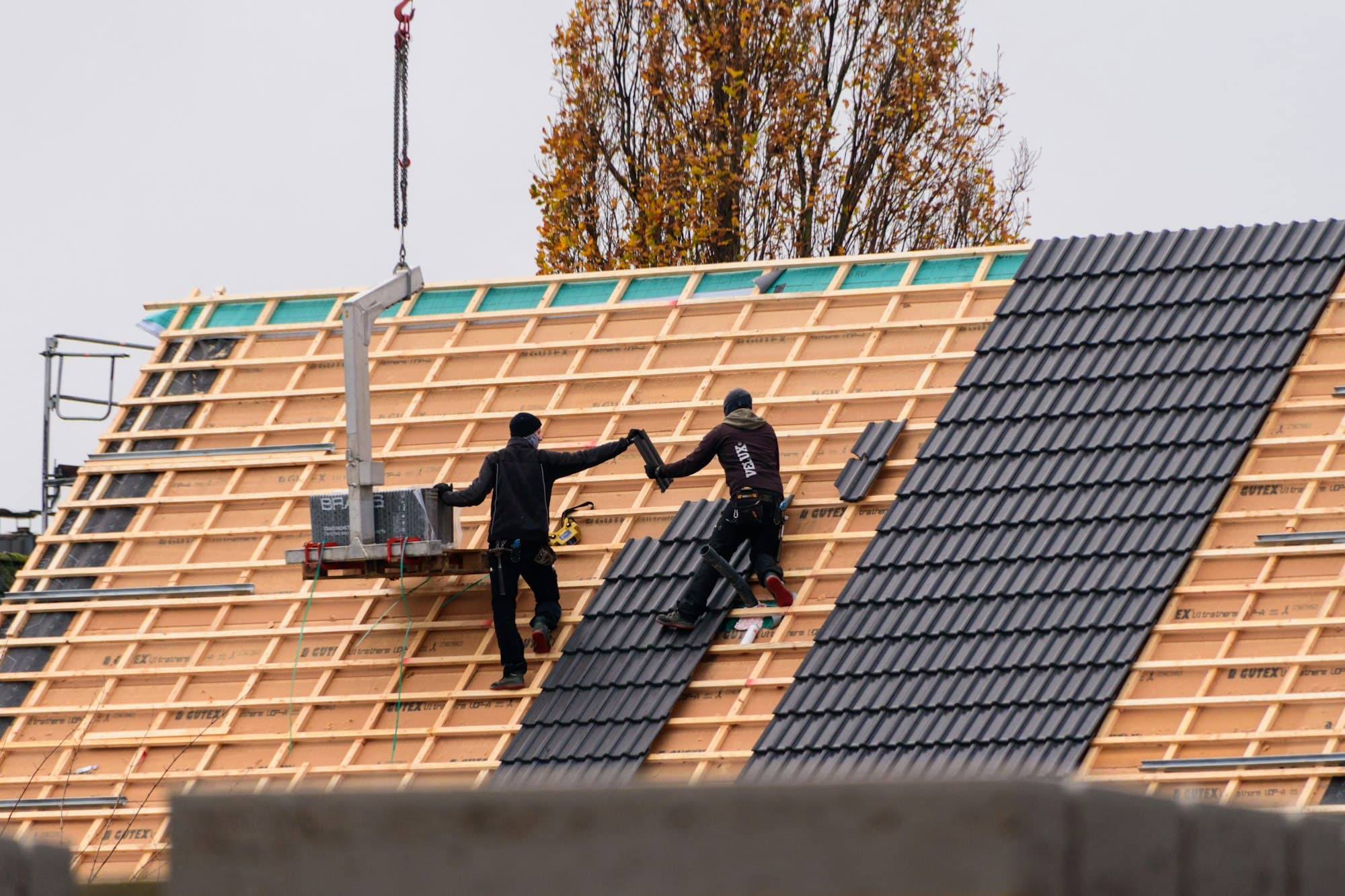 Roofers laying dark tiles across new roof battens