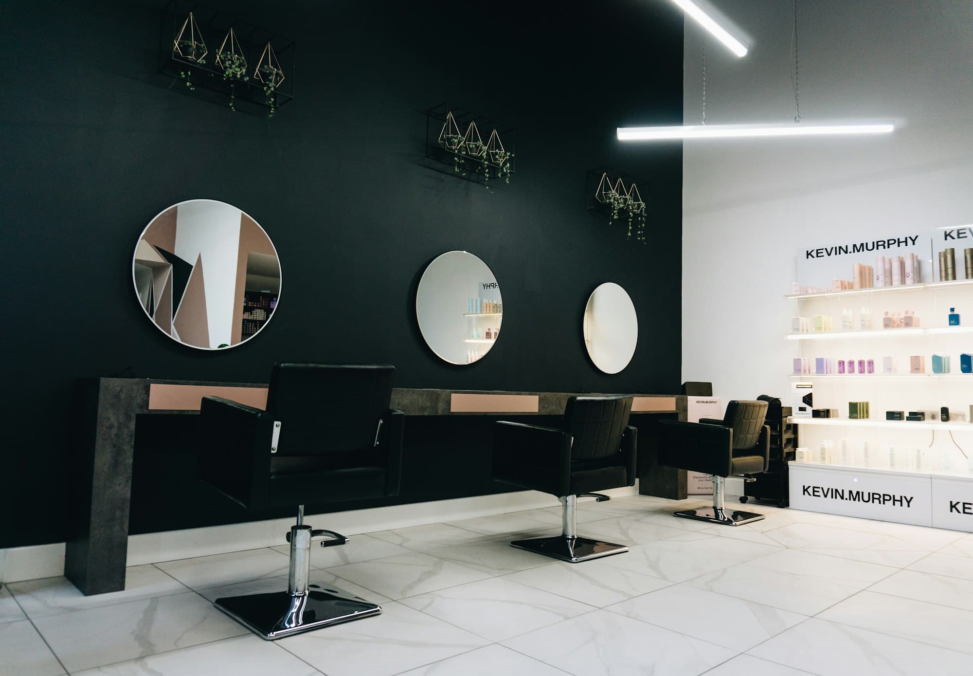 Salon interior with black chairs facing round mirrors on a dark wall